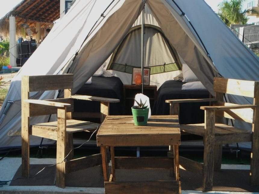 A tent set up outdoors with wooden chairs and a table. A small potted plant sits on the table. Cozy and inviting scene.
